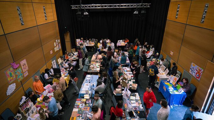 The zine fair from above. There are tables with people sat at them selling their zines. People are browsing the tables.