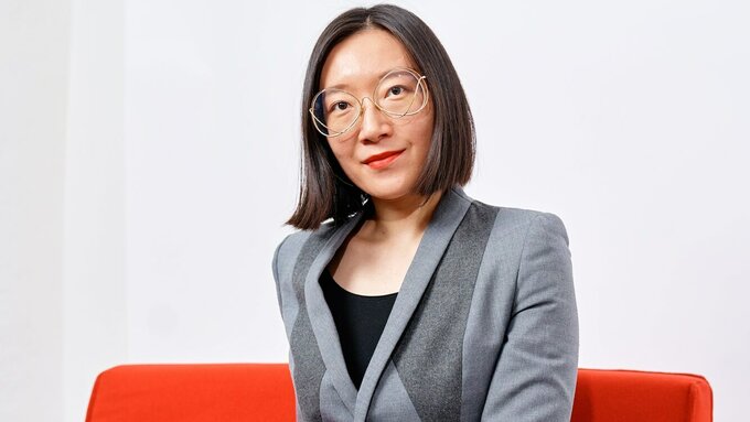 A photo portrait of an East Asian woman wearing a sharp suit and stylish glasses.
