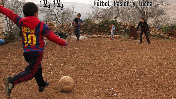 A small boy is kicking a football towards other children. He is wearing a Messi shirt.