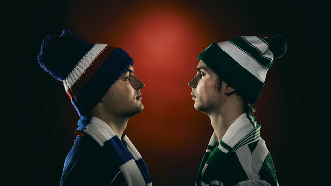 Two stern faced young men stare at each other. One wears Rangers colours, the other Celtic colours.