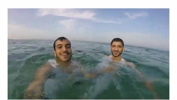 Two men wearing white shirts floating in open ocean. Subtitles read "Good morning, dear Gaza"