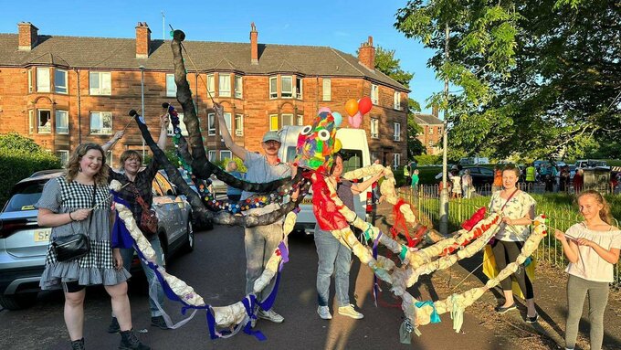 A group of adults and children hold up a large octopus puppet made of colourful fabric.