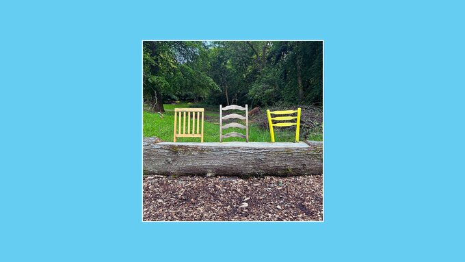 In this image, a tree that has fallen. The backs of three chairs have been attached to the tree trunk creating a bench.
