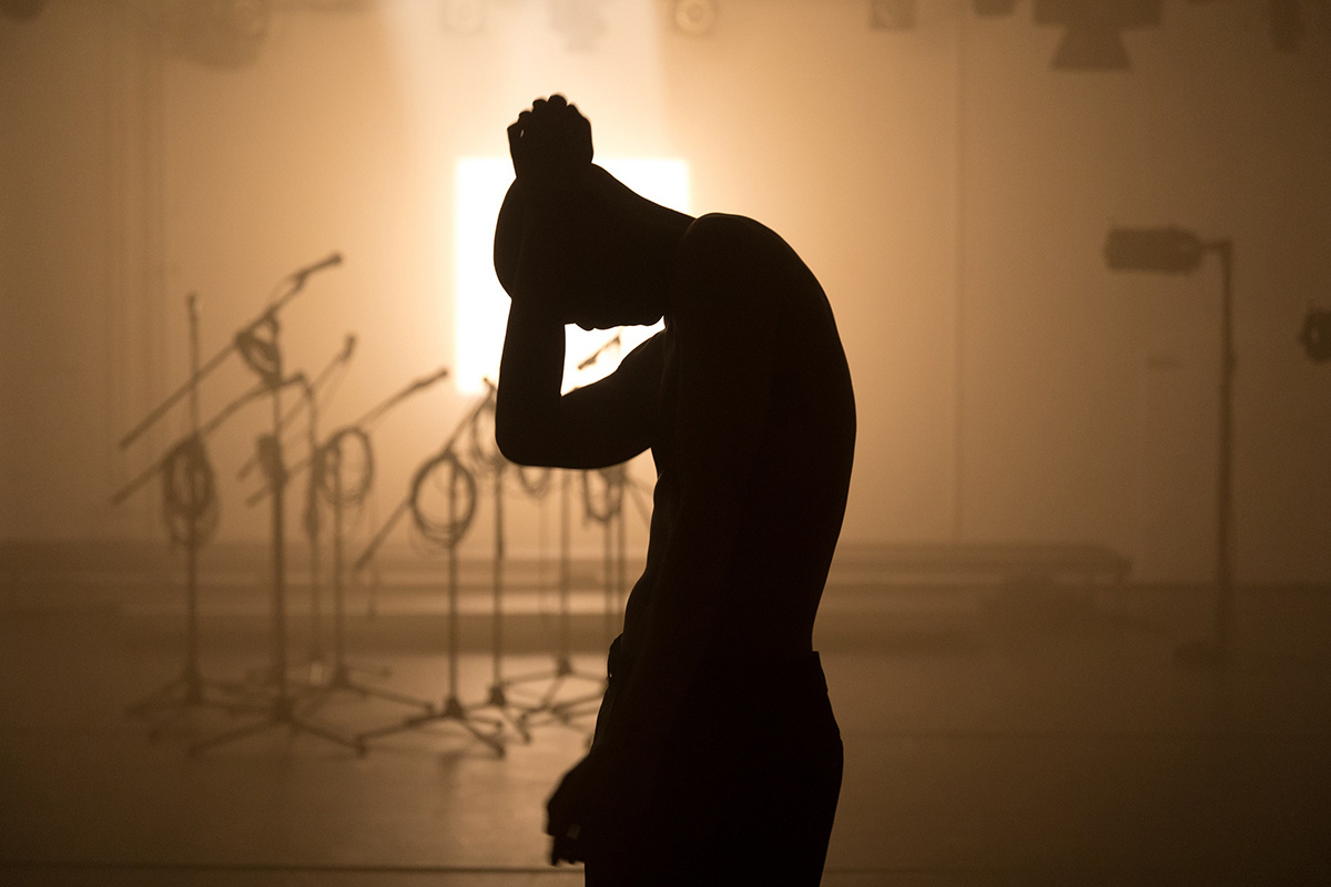 A waist up photo of a person in silhouette, lit from behind in a smoky room. Their arm is raised in the midst of dance.