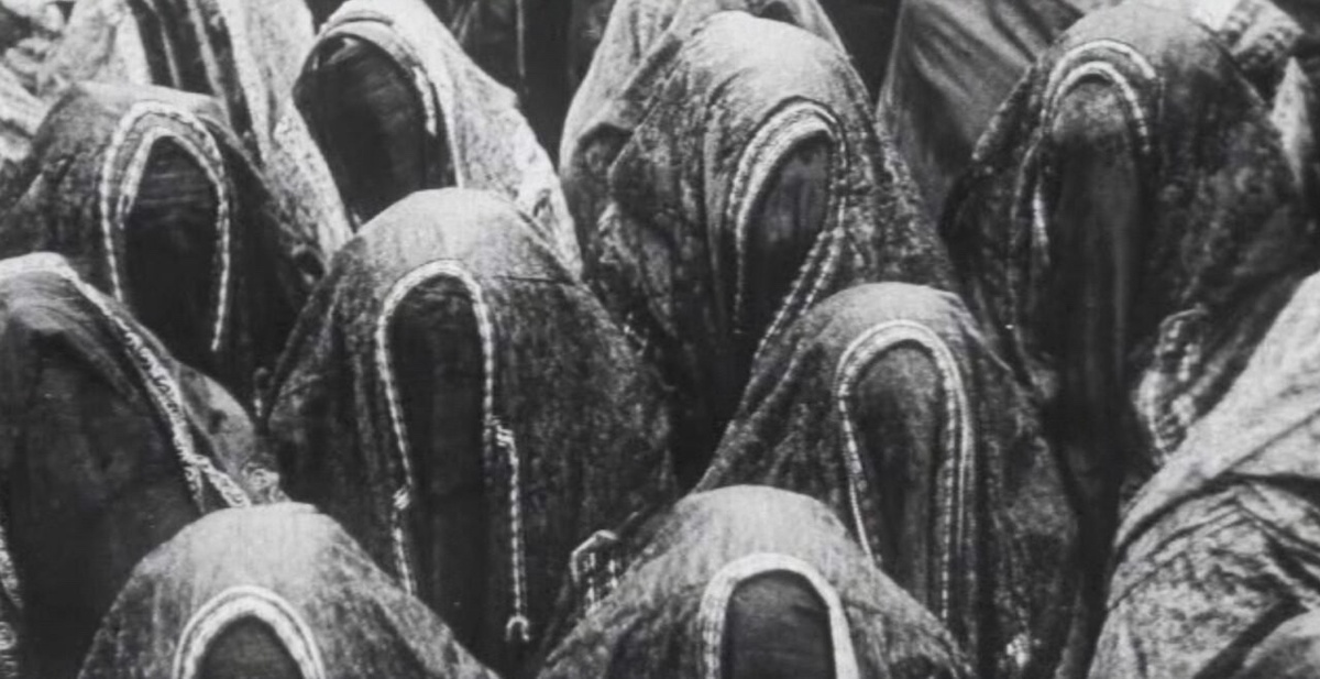 An abstract black-and-white photograph of a crowd of women covering their heads with hijabs.