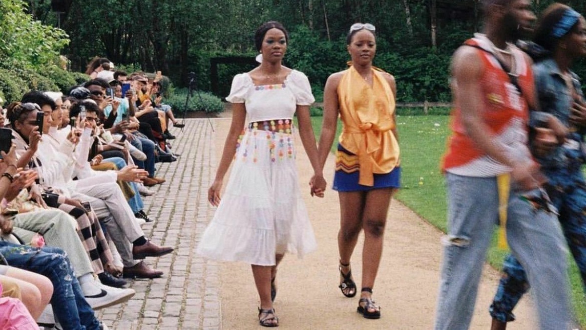 Two Black models make their way down a fashion runway.