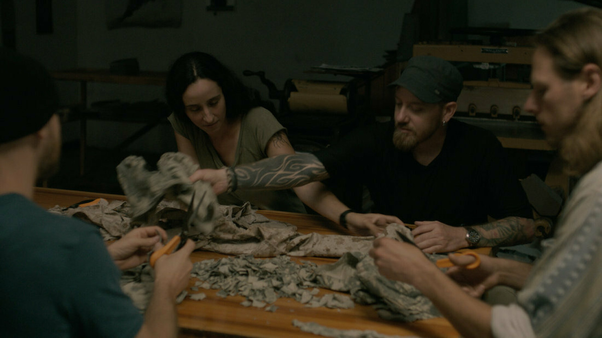 Four veterans, two men and two women sit at a table cutting up their military uniforms.