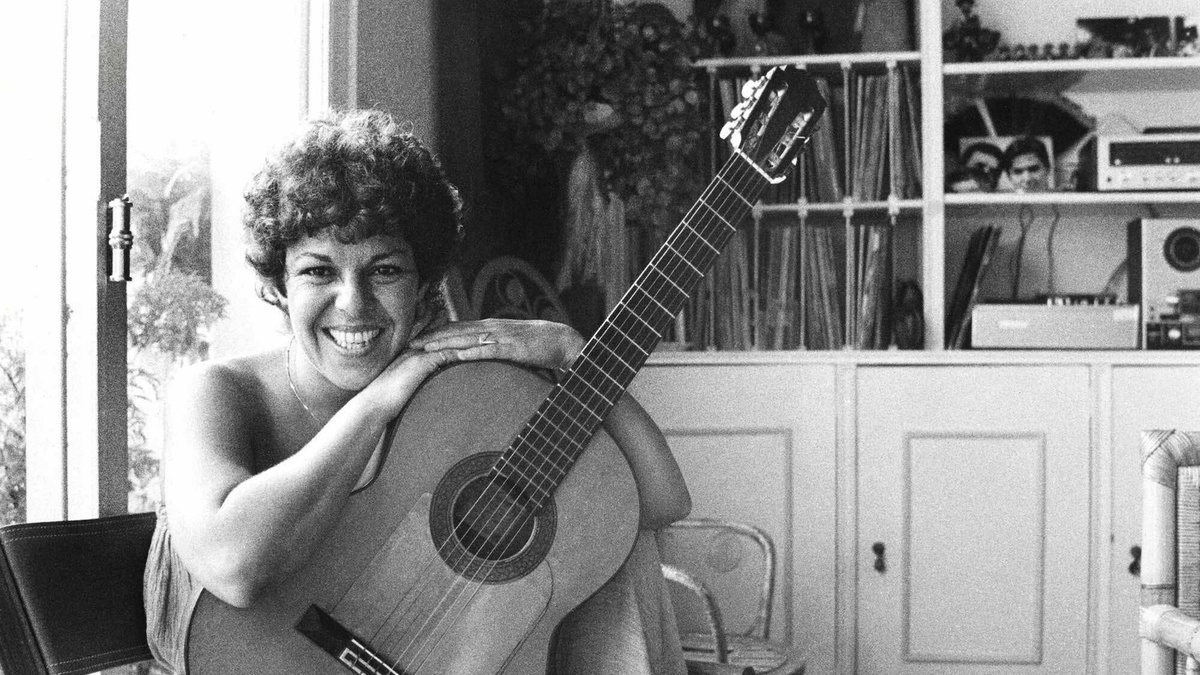 Photo of Heloísa Maria Buarque de Hollanda, known as Miúcha, a mid-40s woman with short curly hair, holding a guitar.