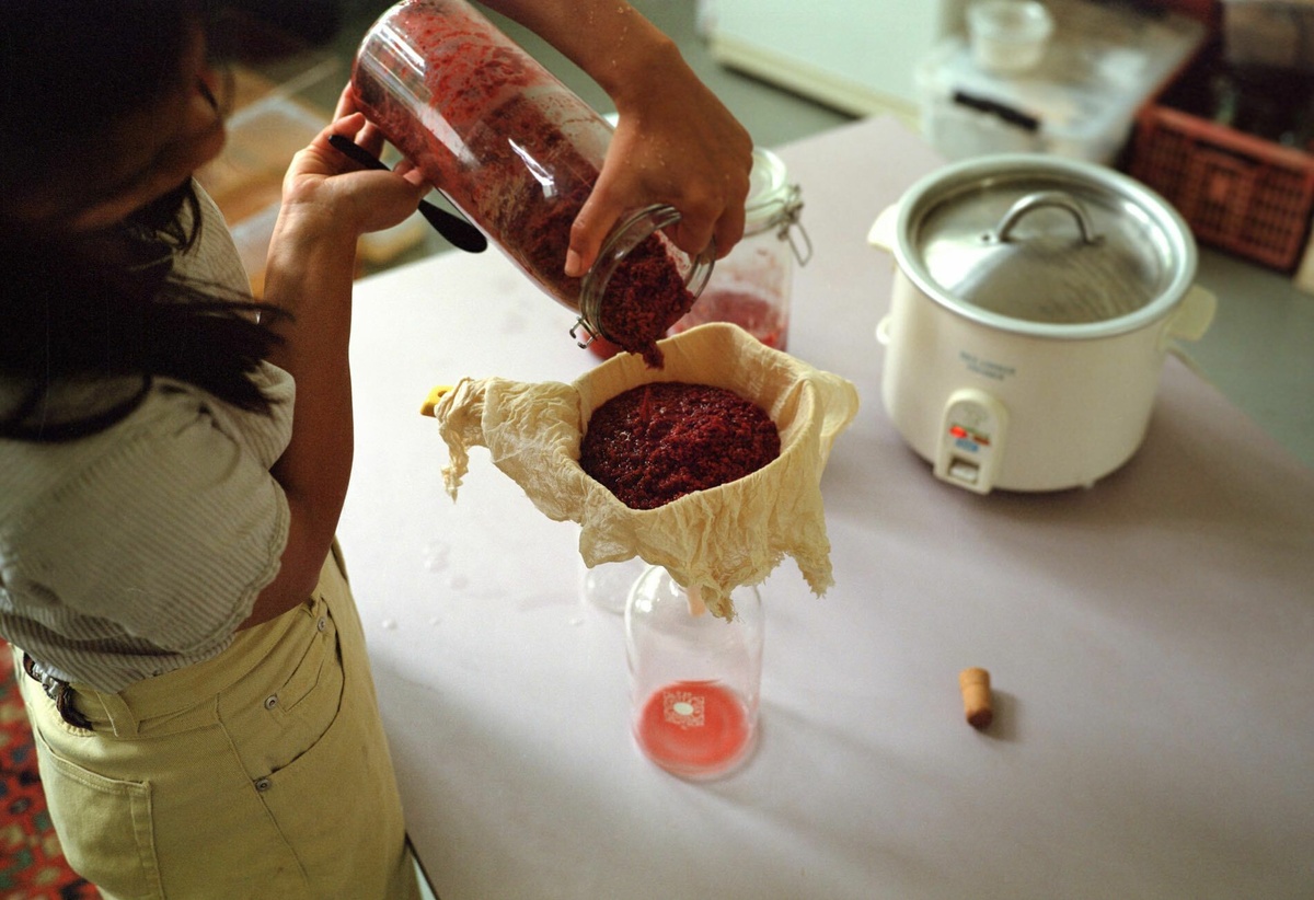 Filtering a thick mass of cooked fruit through a cheese cloth. Delivering a red liquid in the jar.