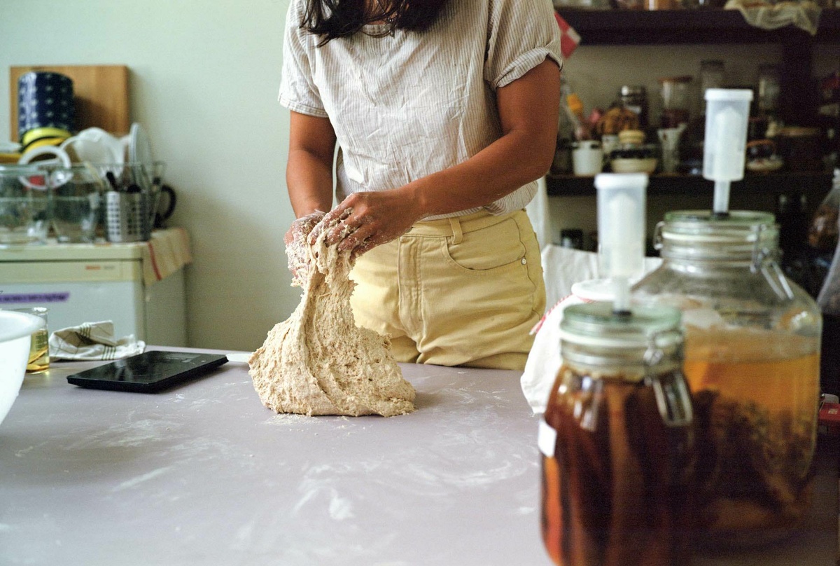 A photograph of Asli Hatipoglu kneading dough in a bright kitchen space, it stretches and bubbles as they work it.