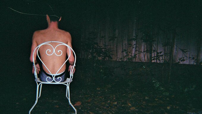 A lone person sits in a garden chair outside at night.