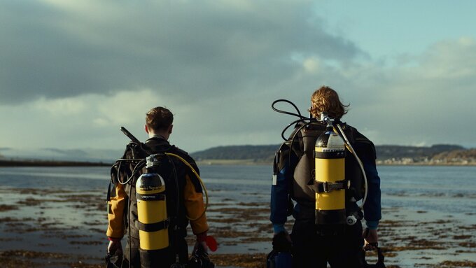 Two divers with scuba packs, stare out into the sea.