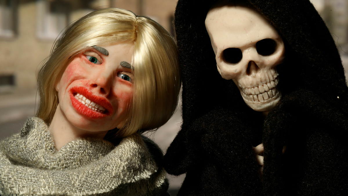 An image of two puppets leaning on eachother. One is a blonde woman with an uneasy smile, the other is the grim reeper.
