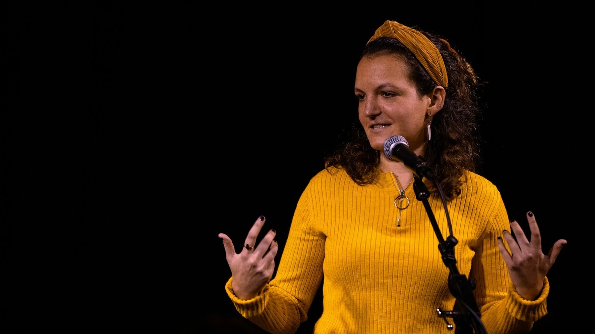 A woman stood in front of a microphone gesturing with her hands.