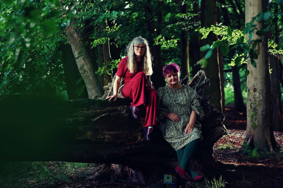 Both women leaning against a fallen tree.