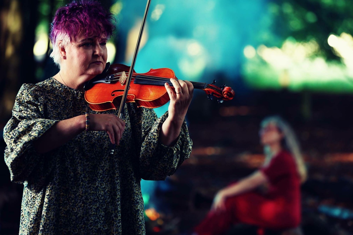 A close up of the woman with short purple hair playing the violin