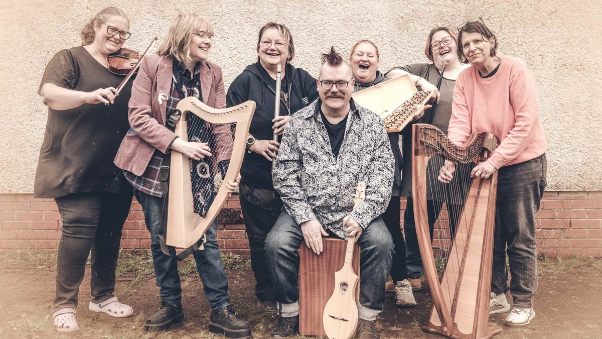 A group of 7 people of various ages with musical instruments laughing and smiling.