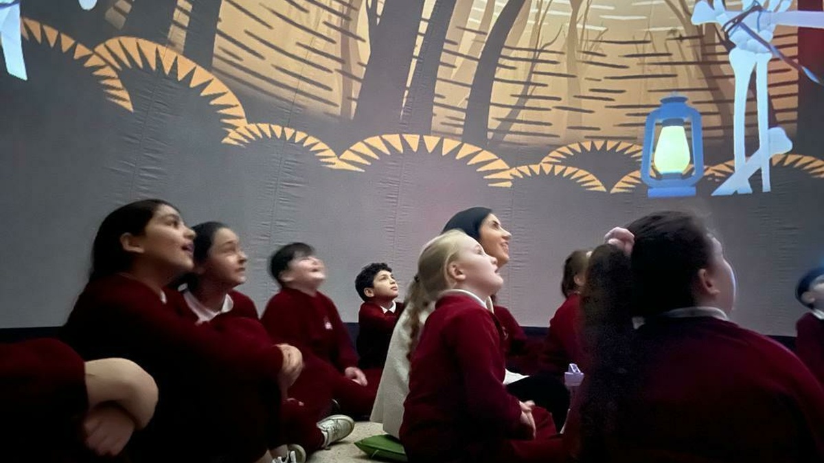A group of children inside a story dome watching the performance, with projected digital images surrounding them.