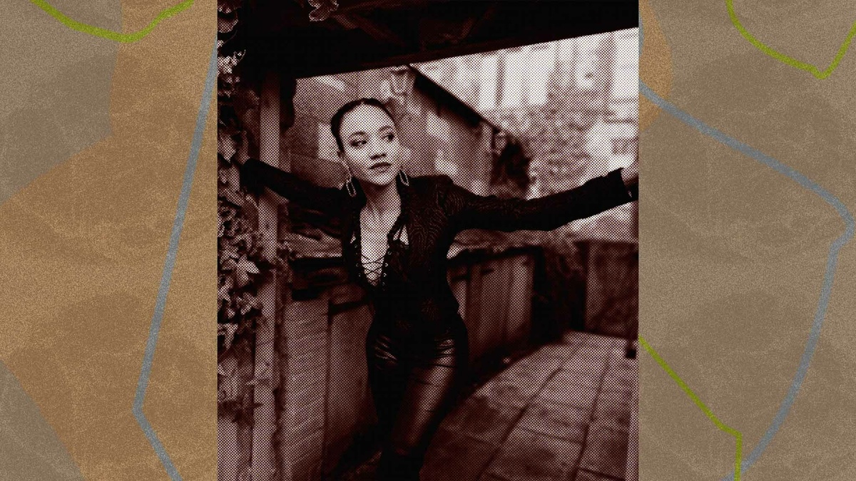 A femme person wearing black clothes leaning through a doorway outside.