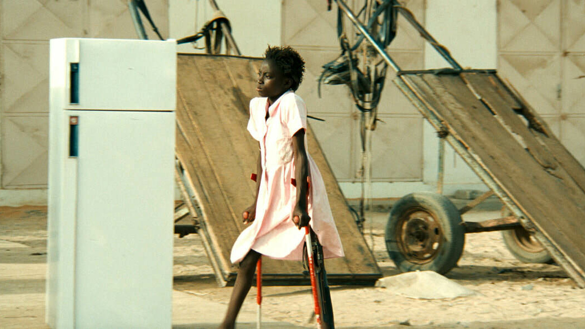 Sili a Senegalese girl, wearing a pink dress and walking through the city on crutches.