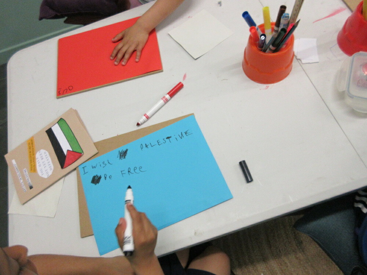 A child's hand writing on a piece of paper "I wish Palestine be free"