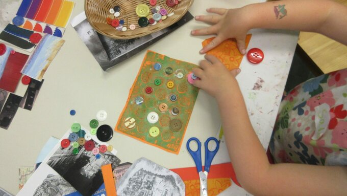 A photo of a child's hands using paper, buttons, and stamps to create an artwork.