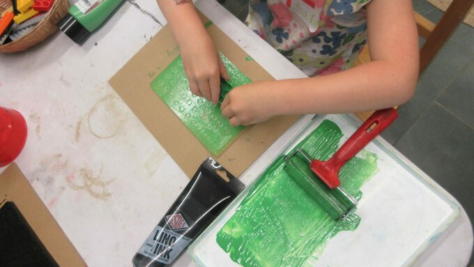 A child's hands creating a print with green ink and an ink roller.