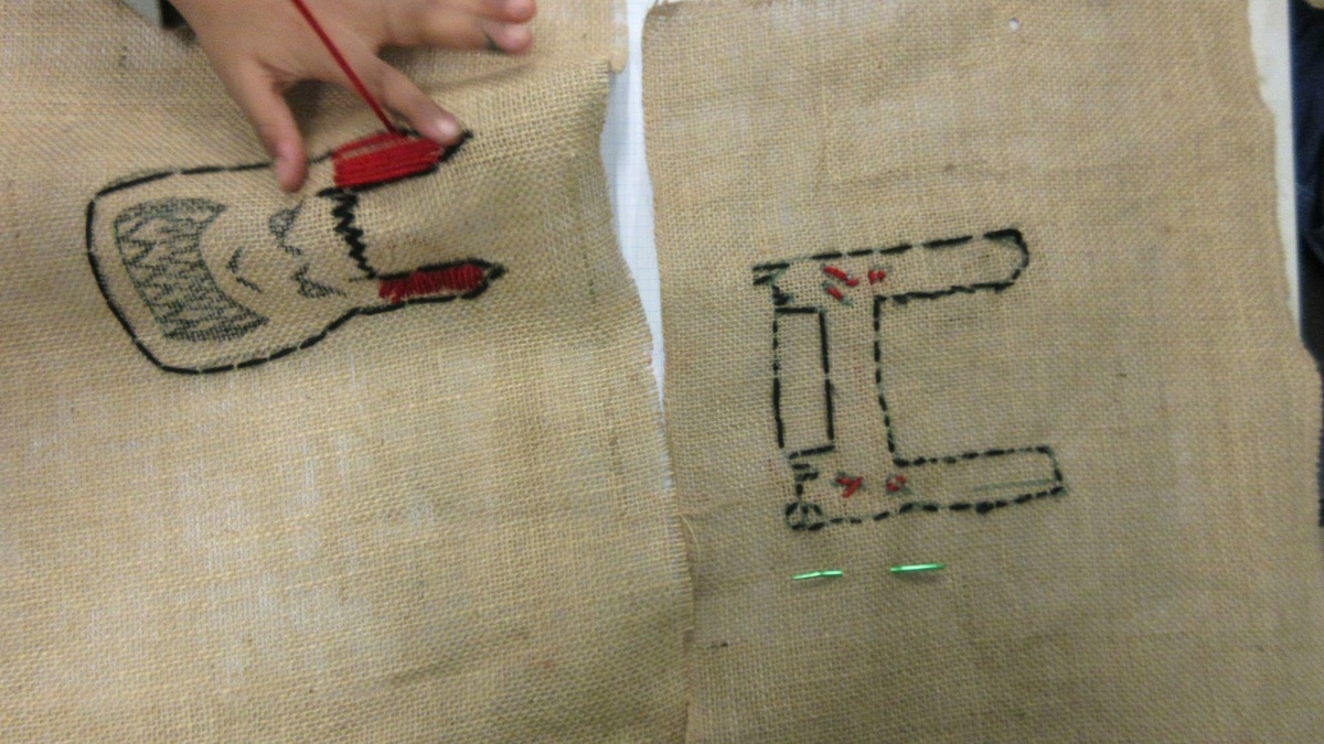 A child's hand stitching a cartoon face on hessian.