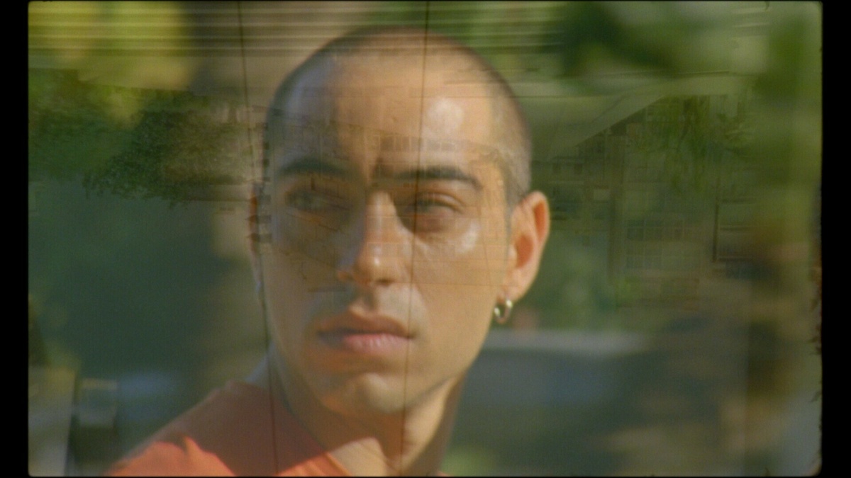 A person with a buzzcut looks to their right in a lightly coloured, slightly blurred image.