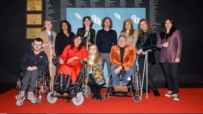 A group of people gather on a red carpet infront of a BFI screen.