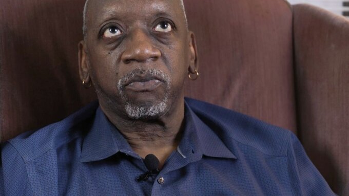 A man in a blue shirt looks up to the cieling from a brown armchair.