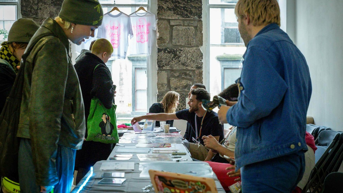 A crowd of people gather round tables with craft items available for sale.