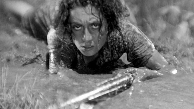 A woman carrying a rifle as she 'army-crawls' through mud and rain.