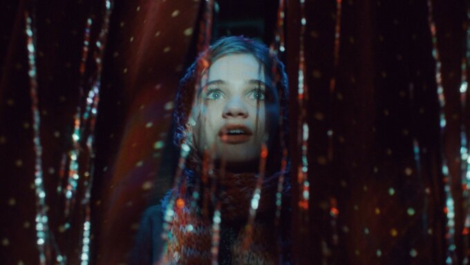 A young woman peering through a doorway shrouded by glittering hanging beads.