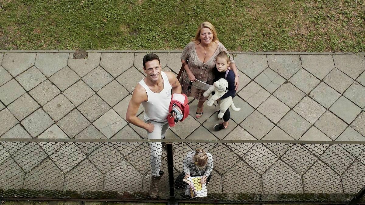 The view from a balcony as a family stand on the walkway looking up and smiling.