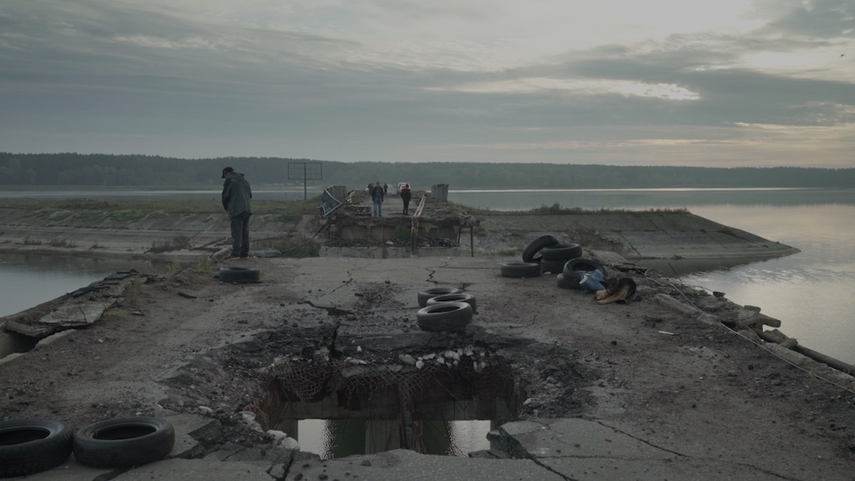 A man stood on a decayed concrete bridge surrounded by old tires and rubble.