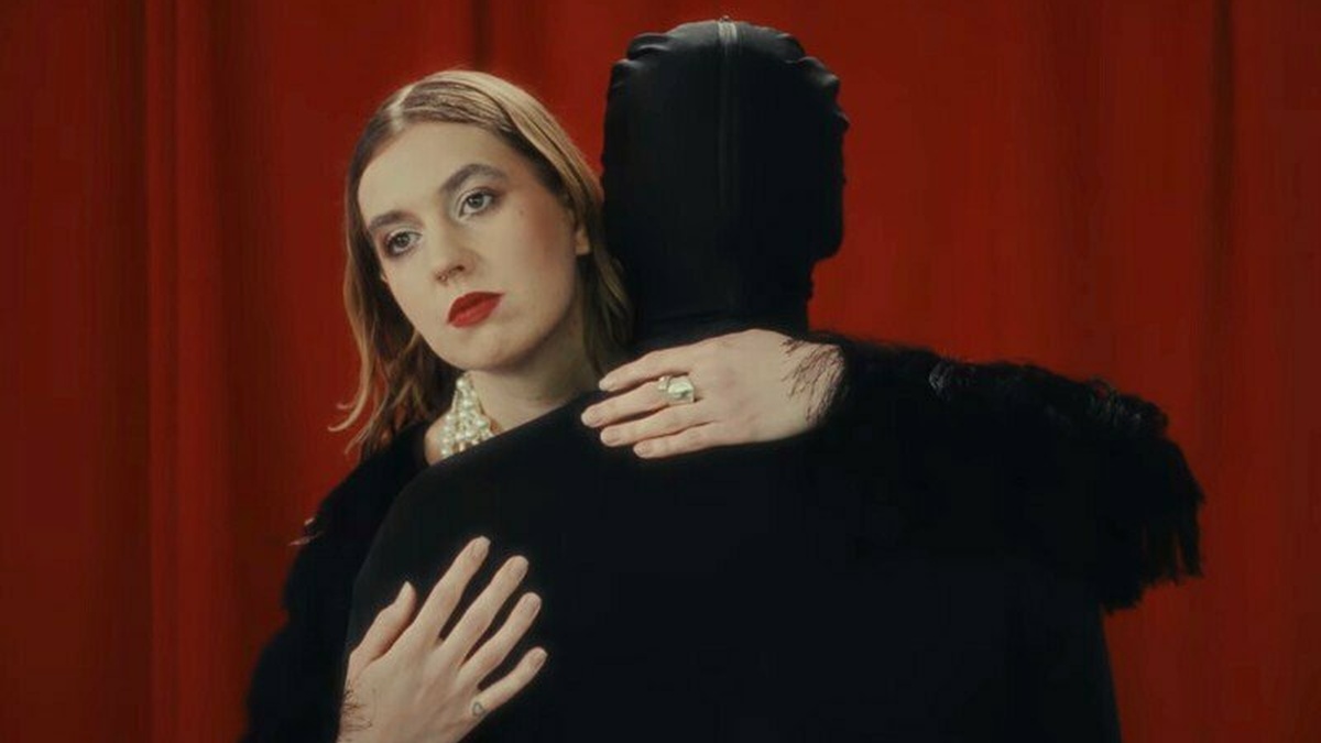 A woman wearing red lipstick hugs a black clothed figure.