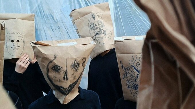 A group of people wearing paper bags with unsettling faces drawn on them.