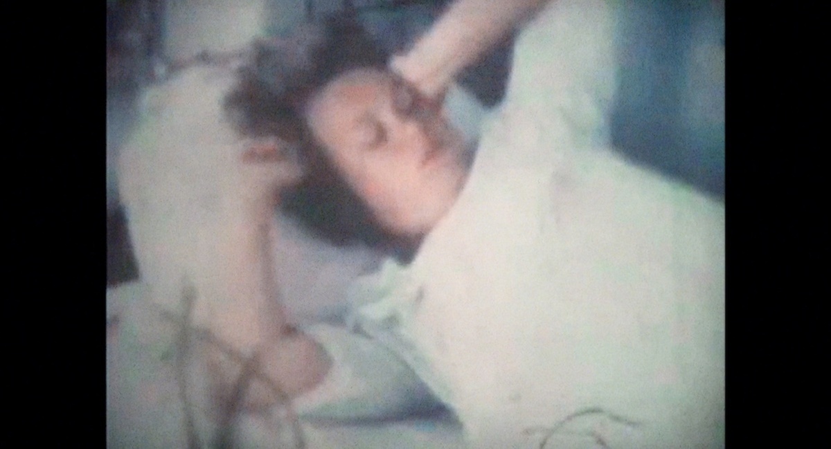 A grainy image of a woman laying in bed with her hands behind her head.