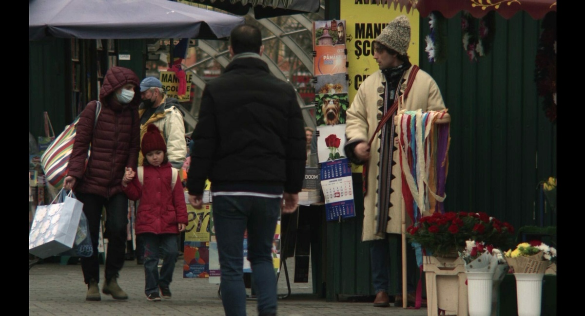 A mother and child walk down a busy street with vendors and newspaper stalls.