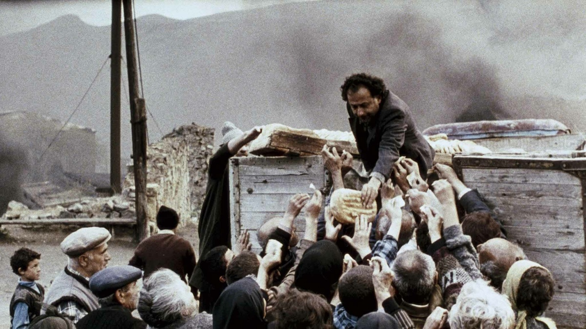 A man handing out bread from a cart to a crowd of people.