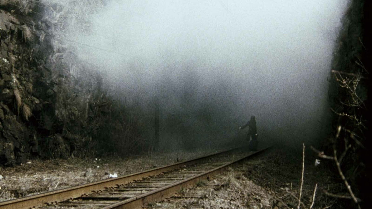 A person walking along a train track into a vast bank of fog.