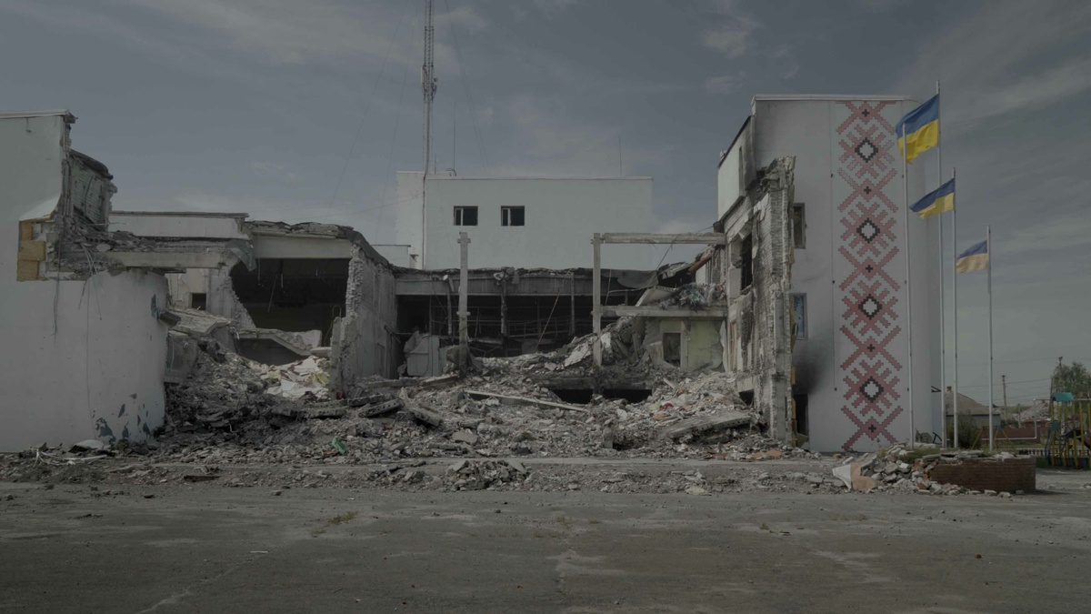 A bombed building with Ukrainian flags flying on still standing flagpoles.