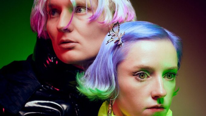 Two fashionable people with dyed hair wearing puffer jackets. The photo is lit by neon green light.