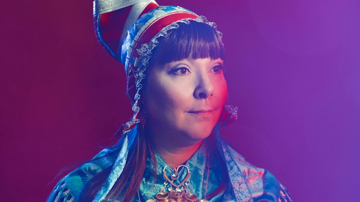 A photo portrait of a woman wearing traditional Sámi dress. Including bright blues, reds, and beaded jewellery.