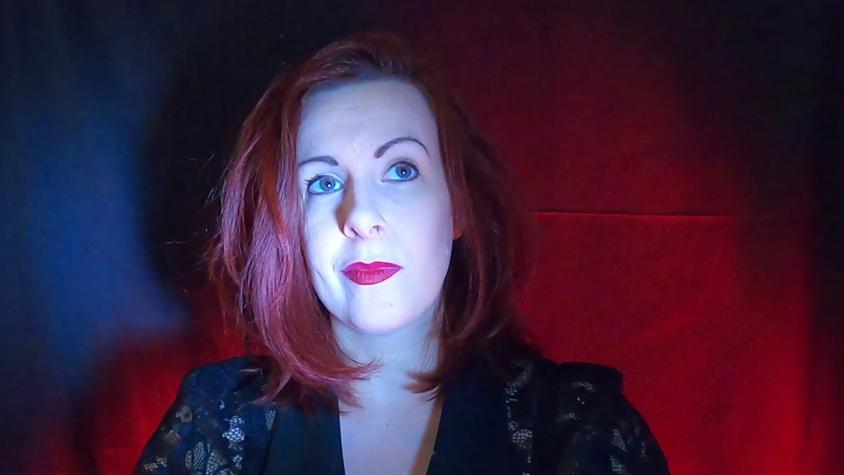 A woman with red hair wearing red lipstick in front of a blue and red background.