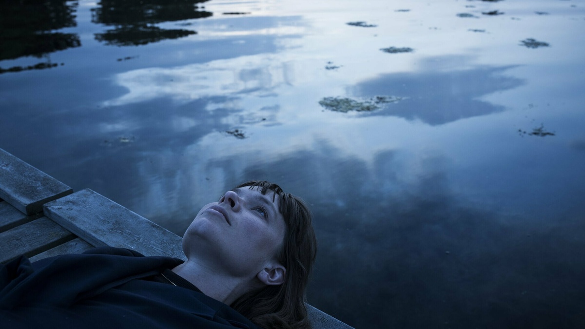 A person laying against a placid reflective body of water outside.