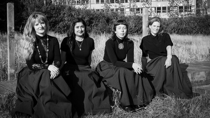 A black and white photo of four women wearing matching pinstriped skirts and black tops.