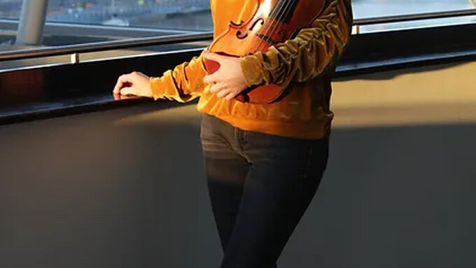 A woman in a sunlit corridor holding a viola.