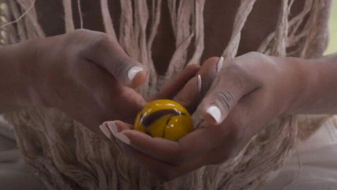 A close-up of hands clasped, holding a yellow and brown marbled ball.